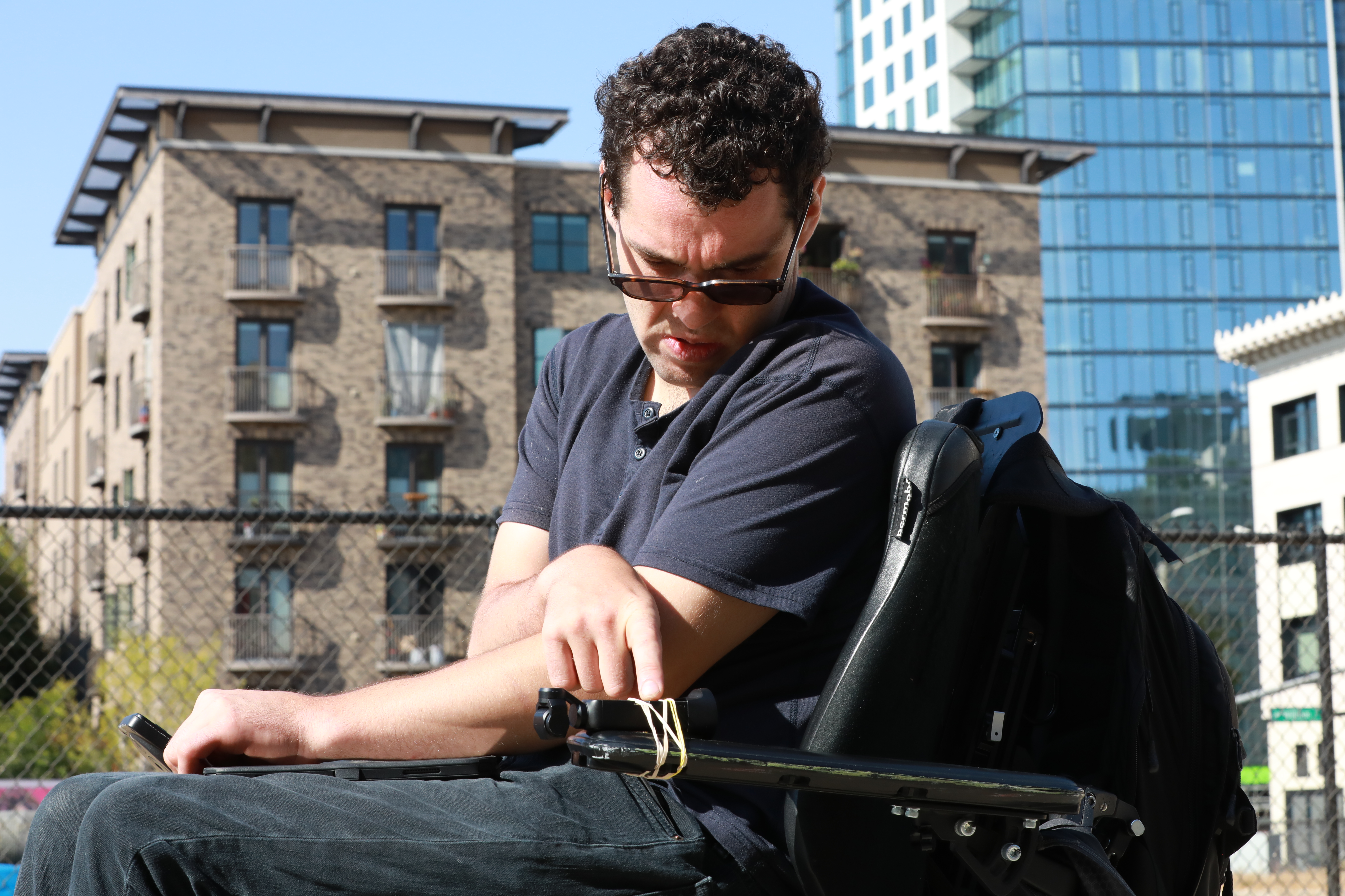 Reid Davenport sits on a wheelchair and presses a button on a camera rubber-banded to the wheelchair's armrest.