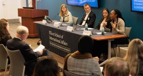 The Elliott School dean and three alumni sit on a panel at the front of a room. 