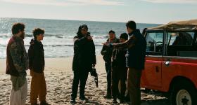 Xavier Manrique stands on a beach with five actors while filming the movie "Who Invited Charlie?"