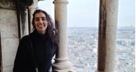 Maha Malik poses next to pillars overlooking a city. 