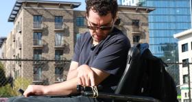 Reid Davenport sits on a wheelchair and presses a button on a camera rubber-banded to the wheelchair's armrest.